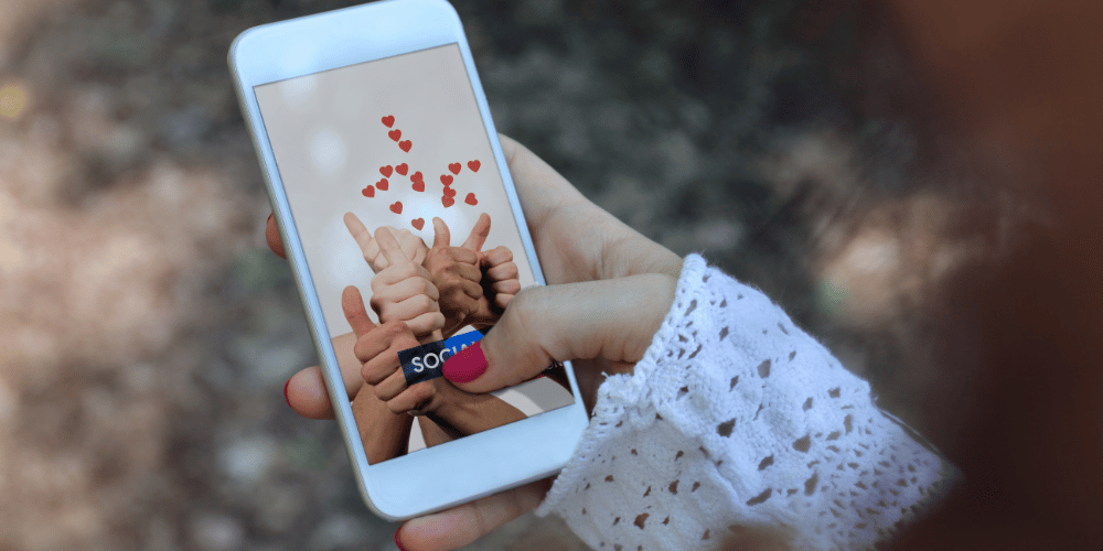 Image of hand holding a mobile phone with screen showing multiple thumbs up and hearts indicating social media likes