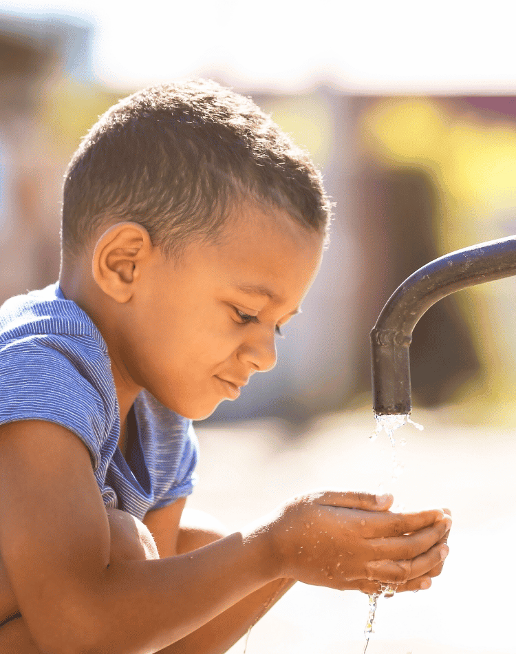 Little boy holding water in his hands from an outside faucet