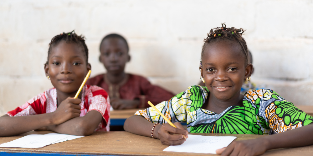 two children sitting at desks with pencils in their hands