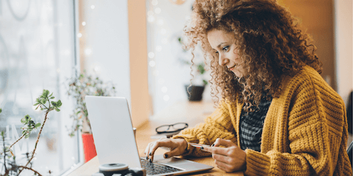 Image of a woman potentially donating to a nonprofit online as she holds a credit card and looks at her laptop